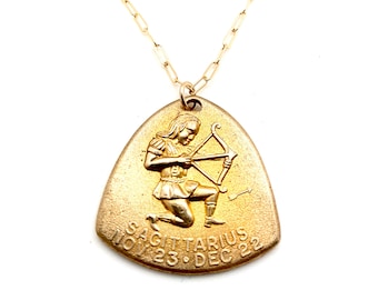 May include: Gold chain necklace with a gold pendant featuring a Sagittarius zodiac symbol. The pendant is shaped like a teardrop and has the text "SAGITTARIUS NOV 23. DEC 22".