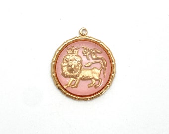 May include: A gold-toned pendant with a pink cameo featuring a lion with a crown. The lion is surrounded by a gold-toned frame.