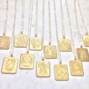 May include: Twelve gold necklaces with square pendants featuring zodiac signs. The signs include Aries, Taurus, Gemini, Cancer, Leo, Virgo, Libra, Scorpio, Sagittarius, Capricorn, Aquarius, and Pisces.