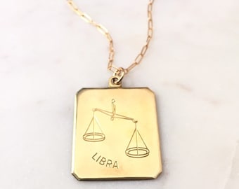 以下が含まれることがあります： 天秤座のシンボルと「LIBRA」という文字が刻まれた正方形のペンダントが付いたゴールドネックレスです。