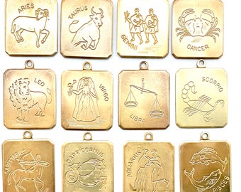May include: Twelve gold-toned metal charms, each featuring a different zodiac sign. The charms are square-shaped with rounded corners and have a loop at the top for hanging. The signs are Aries, Taurus, Gemini, Cancer, Leo, Virgo, Libra, Scorpio, Sagittarius, Capricorn, Aquarius, and Pisces.