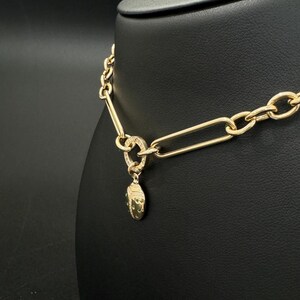 May include: A gold chain necklace with a small, oval-shaped pendant. The pendant is covered in small, green gemstones.