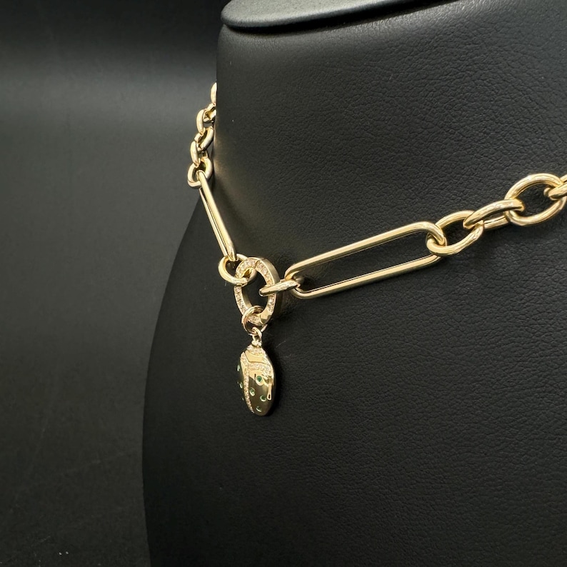 May include: A gold chain necklace with a small, oval-shaped pendant. The pendant is covered in small, green gemstones.