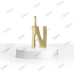 May include: A polished gold-tone metal pendant shaped like the capital letter N. The letter features a smooth, reflective surface and a small vertical loop at the top for attachment. The design is simple, clean, and uniform in its metallic finish.