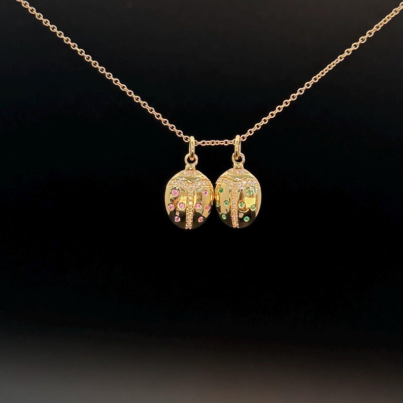 May include: A gold chain necklace with two ladybug pendants. One pendant is decorated with pink and white gemstones, while the other is decorated with green and white gemstones.