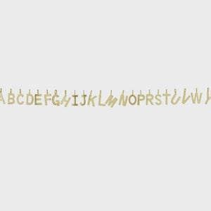 May include: A collection of gold-colored metal letter charms arranged in a horizontal line. Each individual letter pendant features a small loop at the top for attachment, showcasing a simple, clean font style with a polished metallic finish.