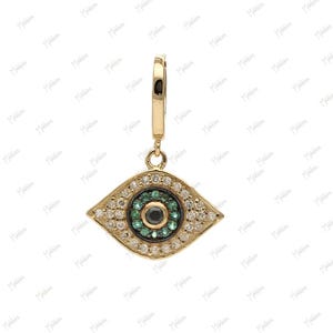 May include: Gold-toned pendant featuring an eye design. The eye is detailed with a black center, surrounded by green and white gemstones. The pendant hangs from a small hoop, suitable for earrings or necklaces. A piece of jewelry.