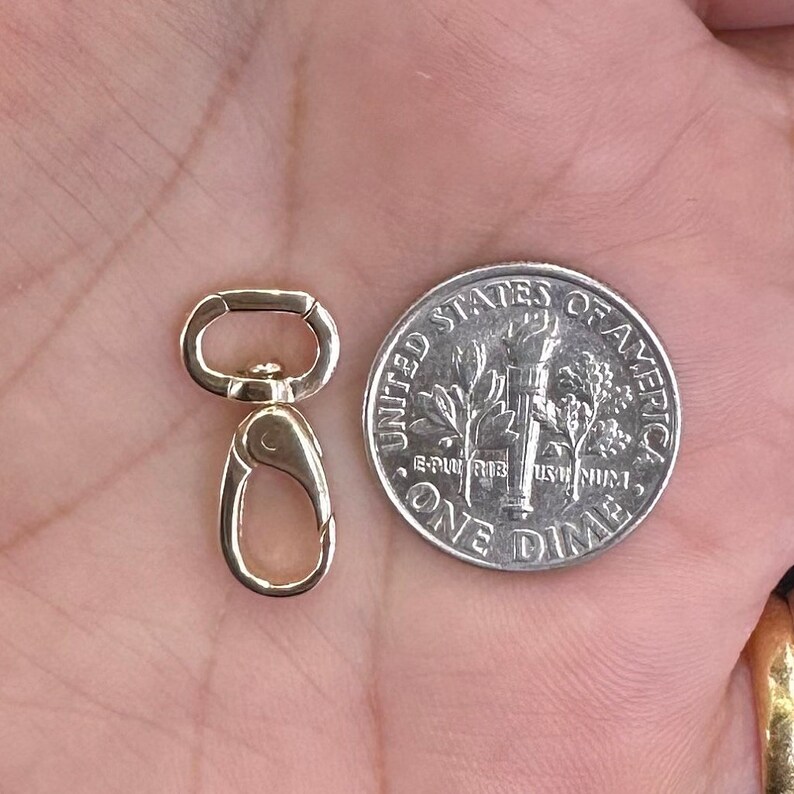 May include: A gold-toned metal swivel lobster clasp with a rounded attachment loop, positioned next to a United States one dime coin for scale. The clasp features a spring-loaded gate mechanism and a smooth, polished metallic finish throughout.