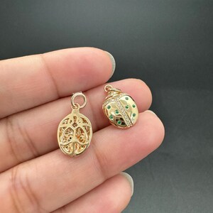 May include: Two gold-toned ladybug charms, one with a detailed openwork design and the other with green and white stones.