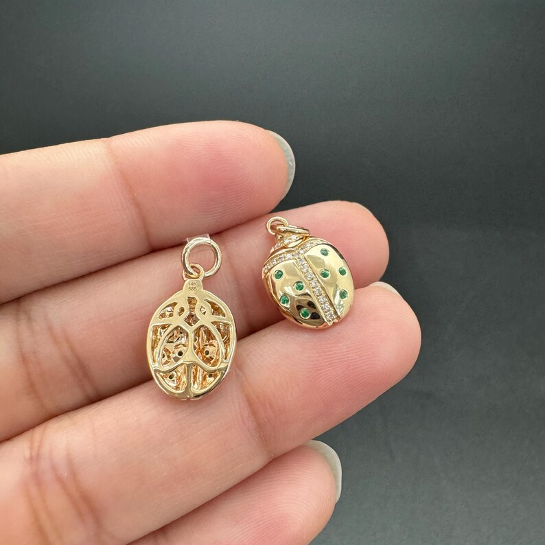 May include: Two gold-toned ladybug charms, one with a detailed openwork design and the other with green and white stones.