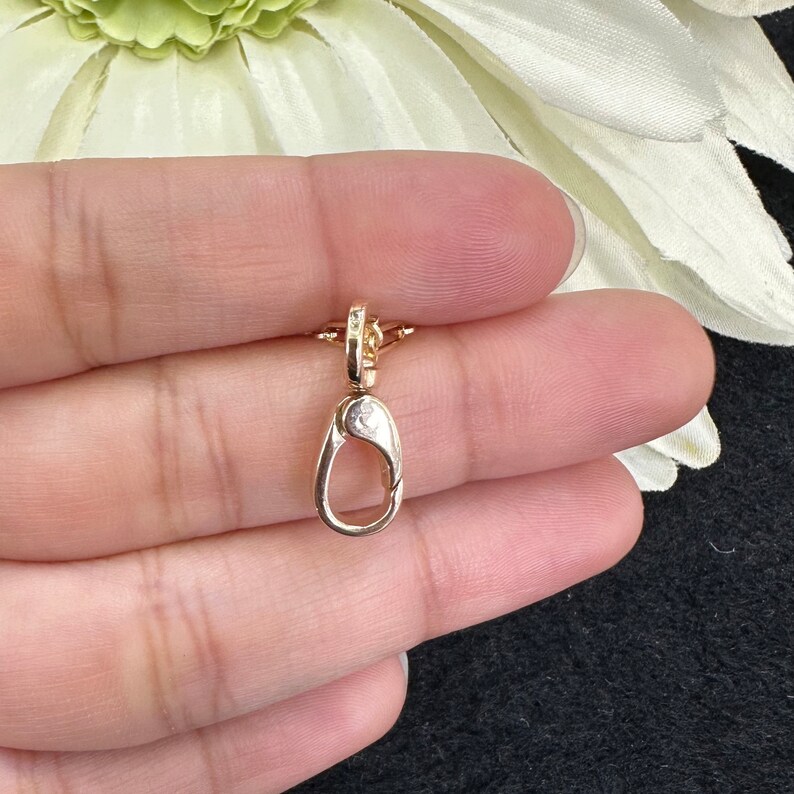 May include: A small gold-toned lobster claw clasp featuring a smooth, polished metallic finish and a spring-loaded mechanism. The jewelry finding has a teardrop-shaped loop at the base and a small swivel attachment point at the top for secure connection.