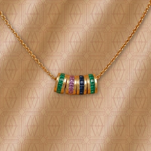 May include: A gold chain necklace featuring a central pendant composed of five cylindrical rings. Each ring is set with a row of square-cut gemstones in alternating colors of green, pink, and dark blue, creating a vibrant, multi-colored design.