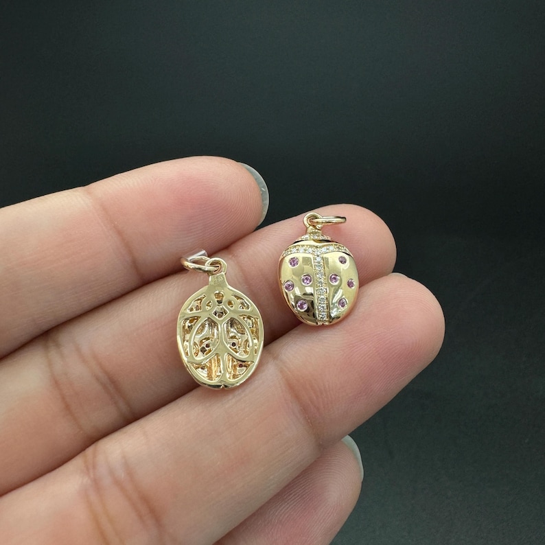 May include: Two gold charms, one shaped like a ladybug with pink and white stones, and the other with a detailed floral design.