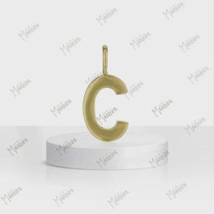 May include: A gold-toned metal pendant in the shape of the uppercase letter C. The pendant features a smooth, polished surface and includes a small vertical loop at the top for attachment to a chain or cord, presented as a single jewelry piece.