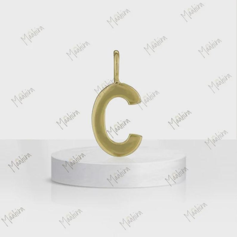 May include: A gold-toned metal pendant in the shape of the uppercase letter C. The pendant features a smooth, polished surface and includes a small vertical loop at the top for attachment to a chain or cord, presented as a single jewelry piece.
