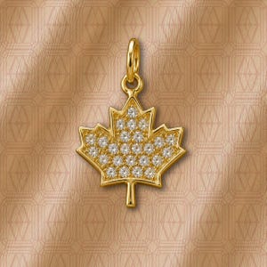 May include: A gold-toned maple leaf pendant featuring a central cluster of clear, round-cut stones set within the metal frame. The pendant includes a small, circular bail at the top for attachment to a chain, showcasing a polished metallic finish.