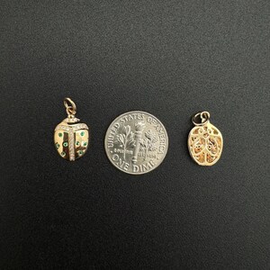 May include: Two gold charms, one shaped like a ladybug with green and white stones, the other a more abstract design, shown next to a US dime for scale.