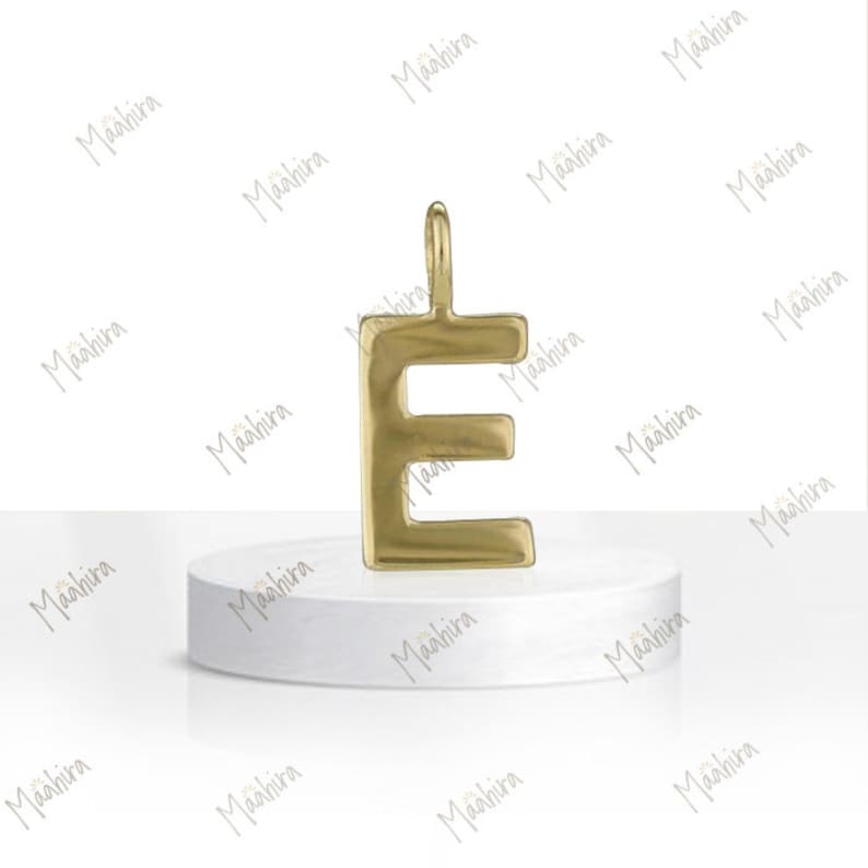 May include: A gold-toned metal pendant in the shape of the uppercase letter E. The pendant features a smooth, polished surface with a rounded bail at the top for attachment. The letter has a block-style font with clean, defined edges.