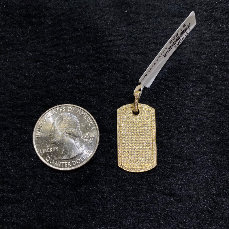 May include: A gold dog tag pendant with a pave setting of small clear stones. The pendant is next to a US quarter for size comparison.