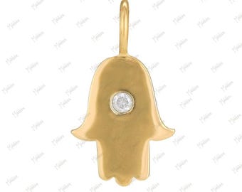 May include: A gold-toned Hamsa hand pendant featuring a smooth, polished surface and a single, small, round, clear gemstone set in the center. The pendant includes a vertical bail at the top for attachment to a chain or cord, with a symmetrical shape.