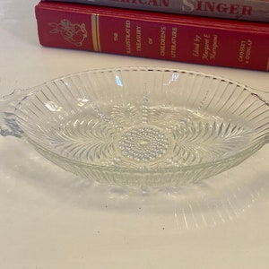 May include: A clear glass serving dish with two handles. The dish has a decorative pattern of lines and swirls.