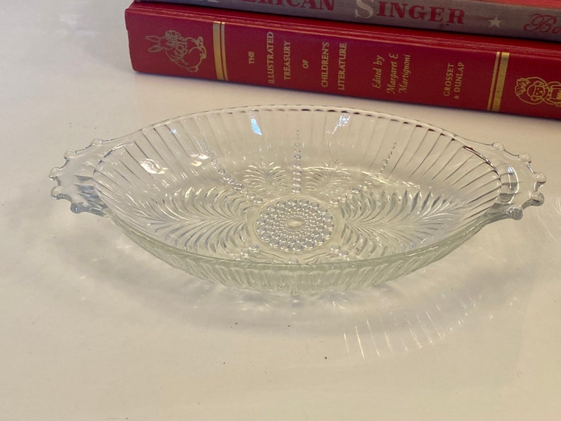 May include: A clear glass serving dish with two handles. The dish has a decorative pattern of lines and swirls.