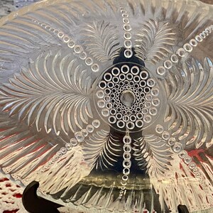 May include: A clear glass serving dish with an etched design of palm leaves and a circle of small dots in the center.