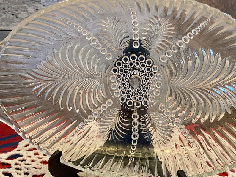 May include: A clear glass serving dish with an etched design of palm leaves and a circle of small dots in the center.