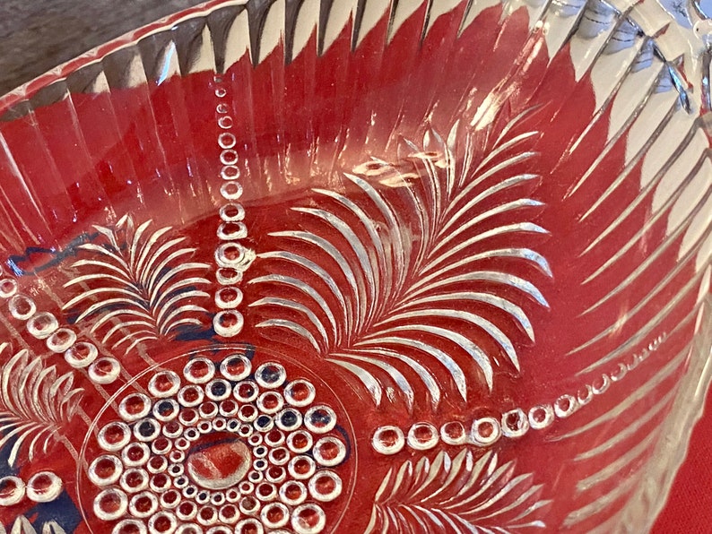 May include: A clear glass bowl with a decorative etched design of leaves and circles. The bowl has a scalloped edge and is perfect for serving fruit or snacks.