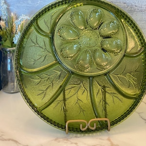 Peut inclure: Un plat de service en verre vert avec un bord festonné et un motif floral. Le plat comporte six sections et une section centrale avec un motif floral. Le plat est sur un support.