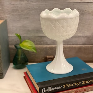 Puede incluir: Tazón de pedestal de vidrio de leche blanco con un patrón de diamante. El tazón está sentado sobre una pila de libros.