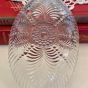 May include: A clear glass bowl with a scalloped edge and a decorative pattern of leaves and dots. The bowl has three small feet.