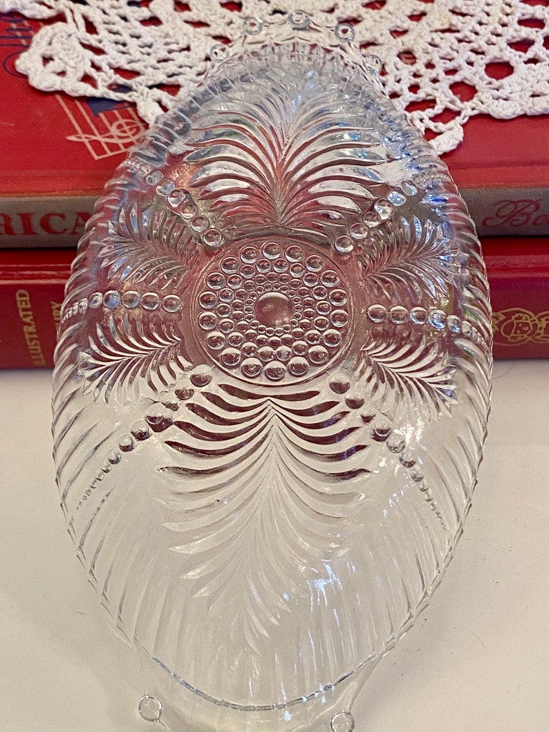 May include: A clear glass bowl with a scalloped edge and a decorative pattern of leaves and dots. The bowl has three small feet.
