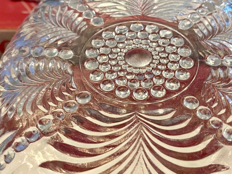 May include: A clear glass plate with a decorative design of a circle of raised dots surrounded by a leafy pattern.
