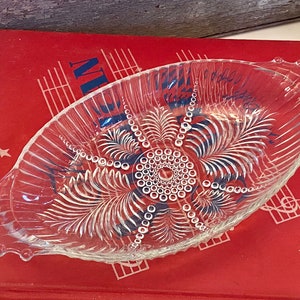 May include: A clear glass serving dish with a scalloped edge and a decorative pattern of leaves and circles. The dish is designed for serving snacks or small desserts.