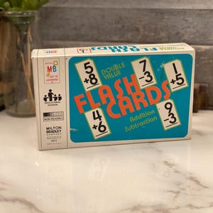 May include: Vintage Milton Bradley "Flash Cards" box for addition and subtraction. The box is teal with orange lettering and white number cards. The box features the MB logo and the words "Double Value".