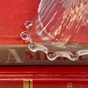 May include: A clear glass bowl with a scalloped edge sits on top of a red book with the word "America" visible on the spine.