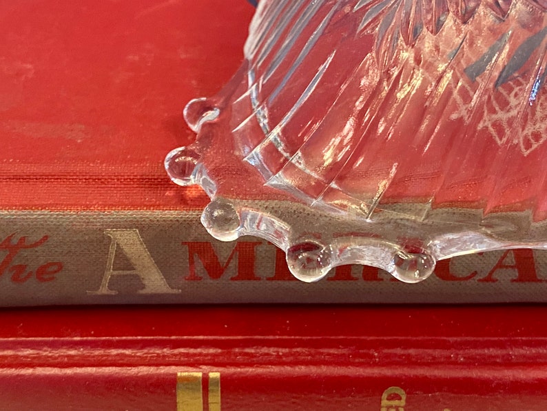 May include: A clear glass bowl with a scalloped edge sits on top of a red book with the word "America" visible on the spine.