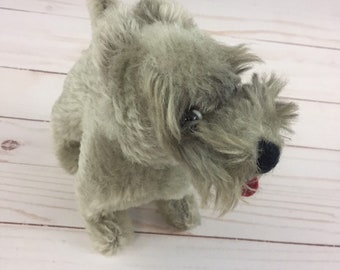 Può includere: Un cane di peluche grigio con la lingua rossa che sporge. Il cane ha un pelo irsuto e occhi neri.
