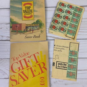 Puede incluir: Un conjunto vintage de libros de ahorro de sellos Top Value. Los libros son amarillos y rojos con el texto "Top Value Stamps" y "Saver Book" en la portada. Los libros están acompañados de una hoja de sellos verdes con el texto "Top Value Stamps" y "10" impreso en ellos.