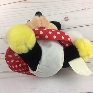 May include: A plush toy of Mickey Mouse wearing a red and white polka dot dress. The toy is lying on its back with its legs in the air.