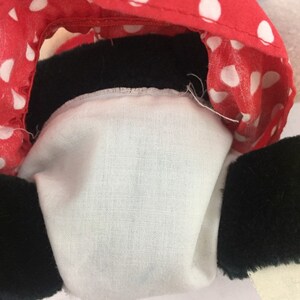 May include: Close-up of a plush toy's head, showing a red and white polka dot fabric with black trim. The toy's face is hidden, but the black fur of the ears is visible.