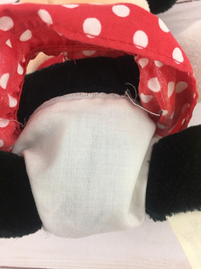May include: Close-up of a plush toy's head, showing a red and white polka dot fabric with black trim. The toy's face is hidden, but the black fur of the ears is visible.