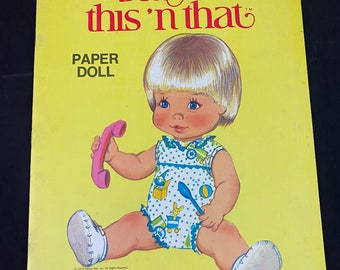 May include: A vintage paper doll book featuring a baby girl with blonde hair. The book is titled "Baby this 'n that" and is a Whitman publication. The cover is yellow with a green and white logo.
