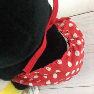 May include: Black and white plush penguin wearing a red and white polka dot dress with a red bow. The penguin has a yellow beak and feet. The tag reads "Little World's".