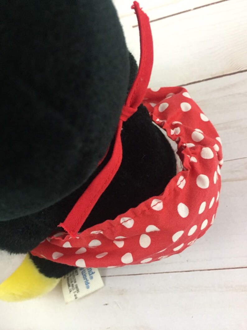 May include: Black and white plush penguin wearing a red and white polka dot dress with a red bow. The penguin has a yellow beak and feet. The tag reads "Little World's".