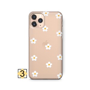 Może przedstawiać: Przezroczyste etui na telefon z złotym tłem i wzorem białych stokrotek. Etui jest przeznaczone do iPhone'a.