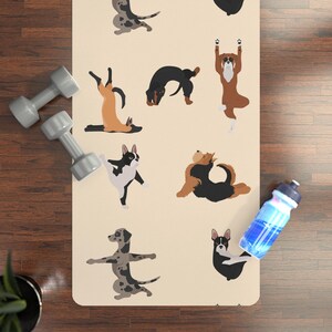 Peut inclure: Un tapis de yoga beige avec des chiens de dessin animé dans diverses poses de yoga. Les chiens sont de couleur marron, noir et gris. Deux haltères grises et une bouteille d'eau bleue sont visibles.