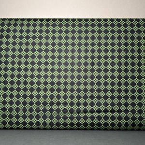 May include: A folded fabric with a repeating pattern of small, green squares set within larger black squares. The fabric has a checkered design, creating a visually interesting texture. The fabric is likely used for sewing or crafting projects.