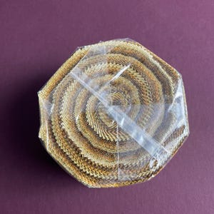 May include: A brown and gold fabric roll with a spiral pattern. The fabric is wrapped in clear plastic.